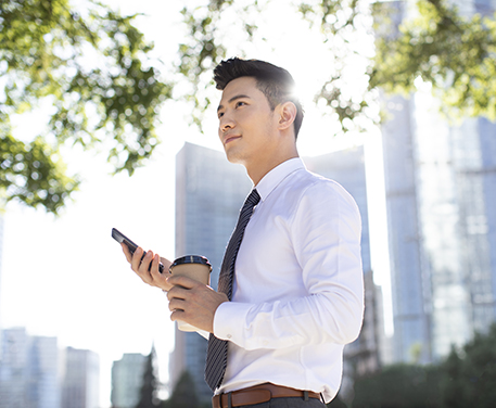 A business person holds a coffee and a smartphone on a sunny day