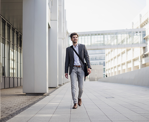 A business person in the CIPM Program walks on a sidewalk between modern office buildings