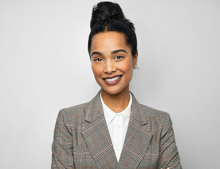 A woman wearing a suit in front of a blank background smiling at the camera